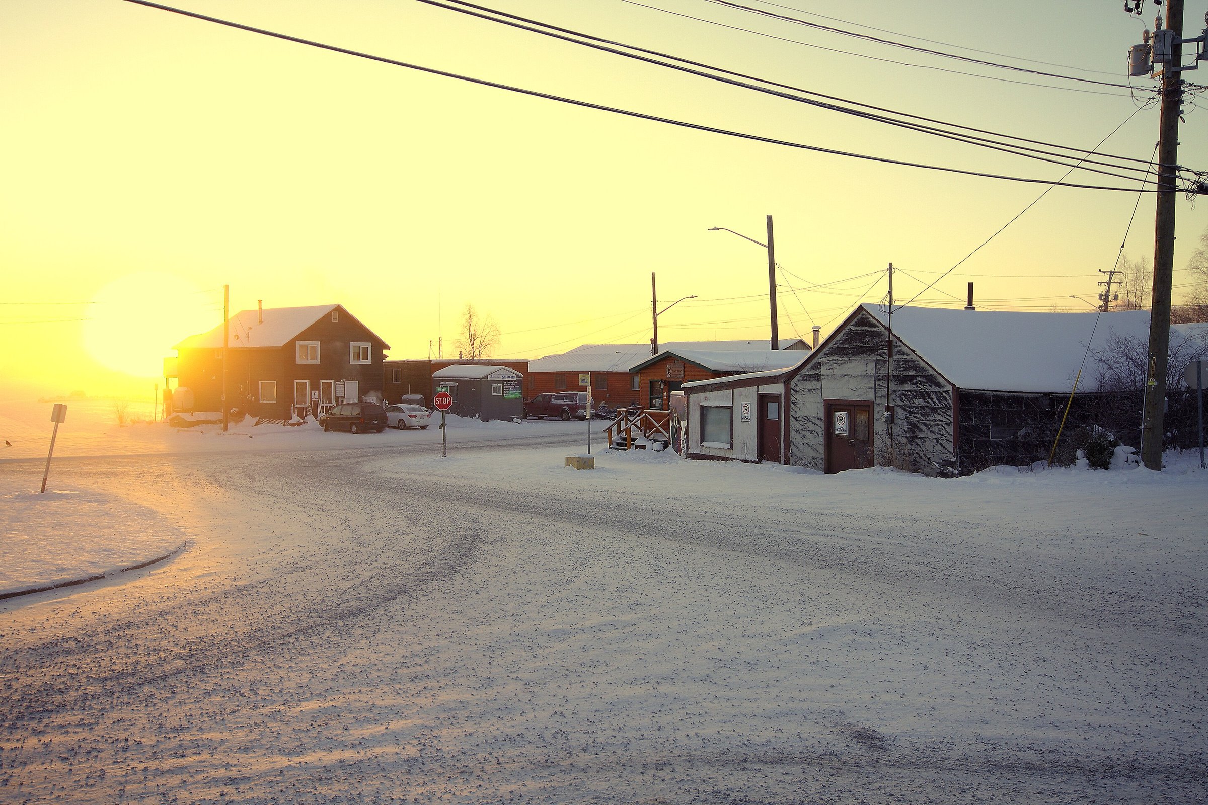 Snow-covered street in Yellowknife’s Old Town at winter sunrise, with power lines overhead